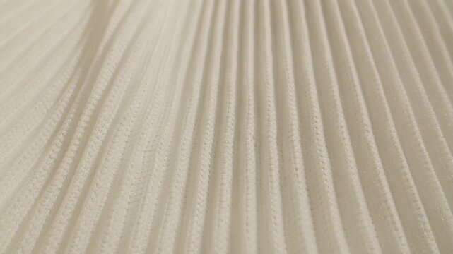 Ribbed fabric texture in cream color, close up of soft pleated knit textile with hand touching, beige knitted cloth background for fashion design and interior upholstery
