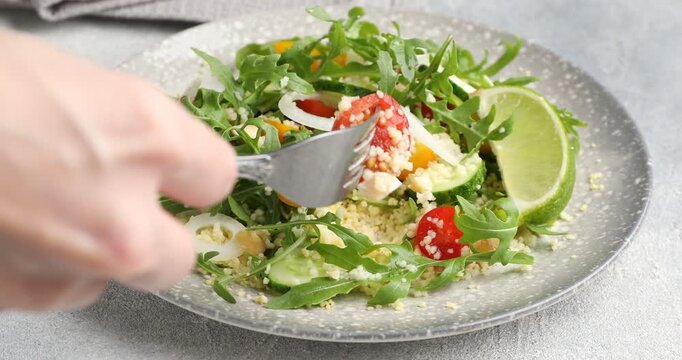 Woman eating tasty salad with couscous at light grey table, closeup