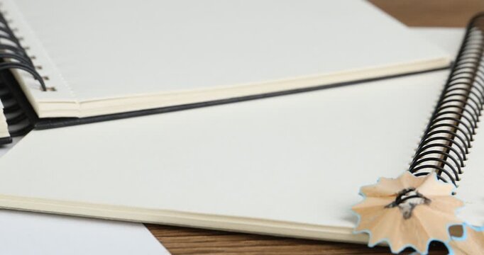 Notebooks, sharp pencils and shavings on table, closeup. Camera moving right
