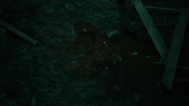 In an eerie, shadowy corner, remnants of tangled netting lie against the uneven ground, hinting at a past activity. Wooden structures loom quietly, adding to the atmosphere of mystery.
