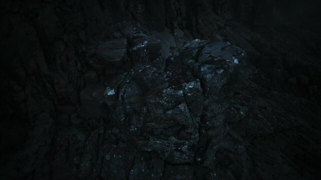 A rocky surface emerges from shadows, showcasing textured layers and patches of lichen. Faint light reveals the details of this rugged terrain, creating an eerie yet captivating scene.