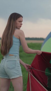 Young woman prepares hot air balloon for flight wearing. With multicolored fabric canopy and casual summer wear. In expansive outdoor area with clear sky elements smiling