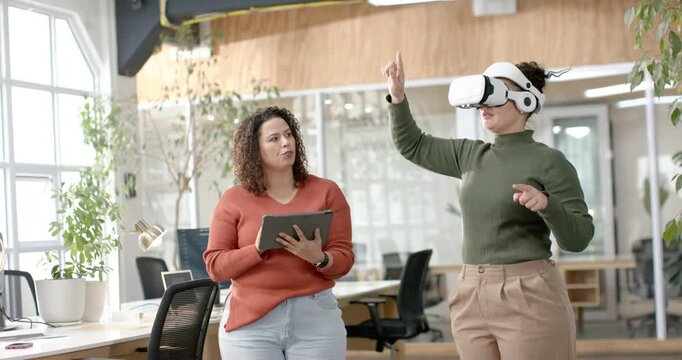 Two female colleagues starting VR demo from tablet in office, VR user pointing, tablet user guiding