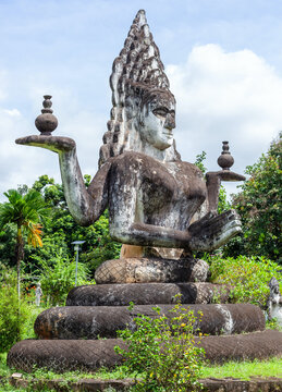 Large weathered statue of a multi-armed deity seated on a coiled serpent at Buddha Park in Laos.