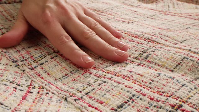 Tweed fabric texture with woman hand touching, close up of multicolor boucle woven textile for coat, luxury wool cloth sample in fashion shop and factory production