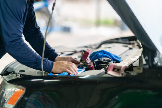 Close-up of an auto mechanic adjusting terminals on a blue car battery under an open hood during vehicle maintenance.