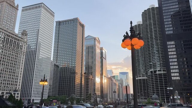 Chicago skyscrapers catch warm sunlight while decorative street lamps glow in the foreground. Tall facades and rows of windows frame a horizontal city view of urban architecture in Illinois, USA.