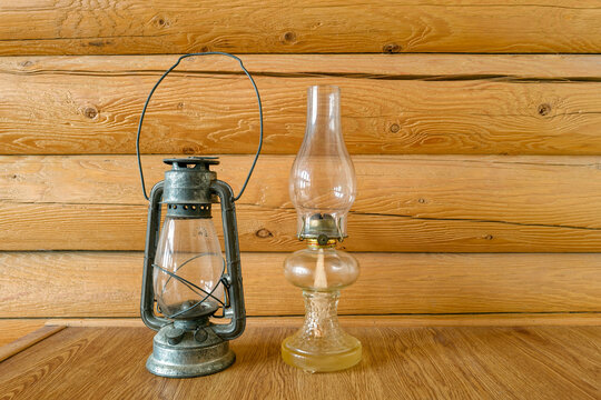 Two antique kerosene lamps displayed by a log cabin wall