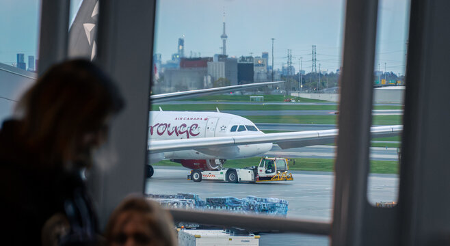 Toronto, Ontario, Canada - 05 26 2026: View through airport terminal window of Air Canada Rouge airplane with pushback tractor on tarmac and CN Tower skyline
