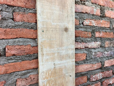 Close up of an unfinished red brick wall with wet cement mortar and a vertical wooden plank as a formwork column at a house construction site, perfect for architecture build photo