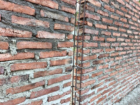 Unfinished red brick wall under construction with an exposed vertical steel rebar column frame in between, ideal for building development, architecture masonry, and house structural photo.