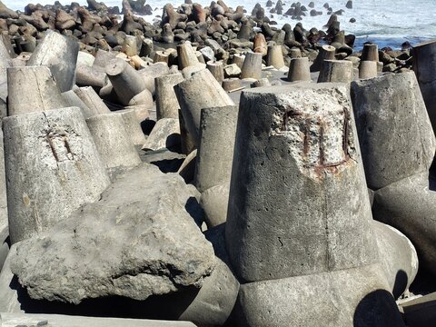 Close up of a broken concrete breakwater tetrapod showing rusted internal steel rebar against a backdrop of coastal waves