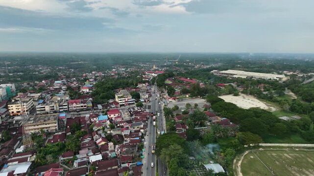 High-angle perspective tracking along a central road dividing a compact community townscape with local buildings and houses. Countryside urban development and lifestyle.