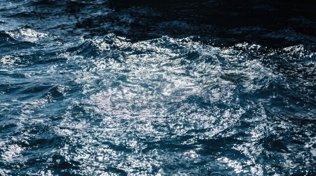 Dark, turbulent water crashes with powerful waves. Sunlight glints off the crests of the waves, creating a dynamic and shimmering effect.