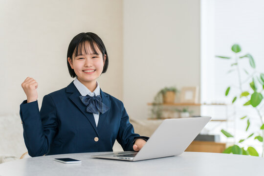 家のリビングでパソコンを使いながら笑顔でガッツポーズをする制服姿の女子高校生