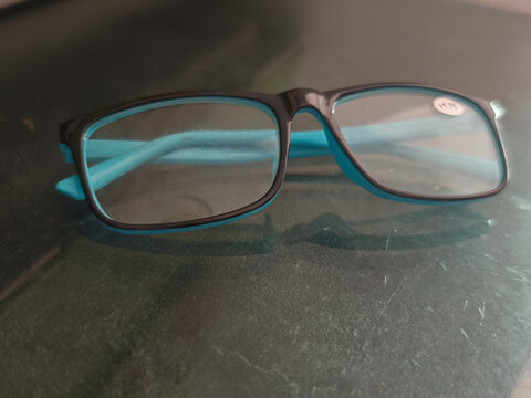 modern blue and black reading glasses resting on a textured, scratched surface. Target audience Optometry clinics, vision care articles, senior health publications, and educational materials requiring