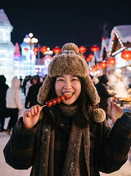 Happy woman eating tanghulu candied hawthorn at Harbin Ice and Snow Festival