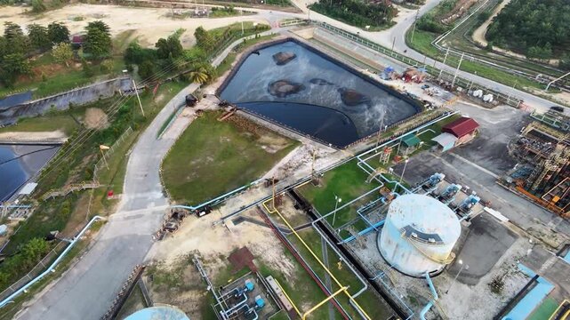 Aerial view of an industrial wastewater treatment facility with storage ponds and processing tanks near an industrial plant under a clear sky. Environmental management and industry concept.