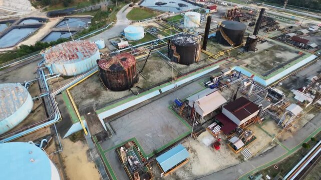 Aerial view of an industrial processing plant and oil refinery facility featuring large storage tanks, piping networks, and processing units under daylight. Industry and energy concept