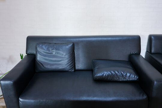 Black leather sofa with cushions against white brick wall, creating modern living room interior with comfortable seating and soft natural light