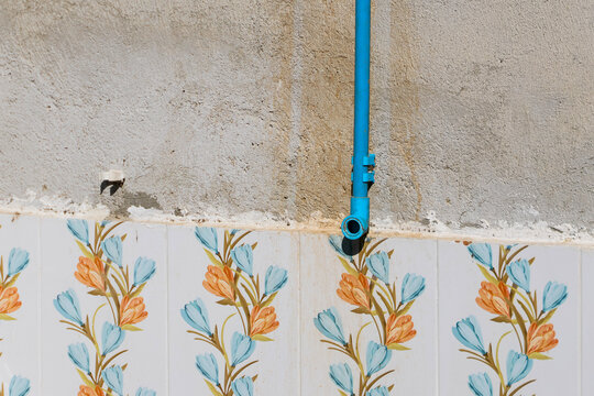 Blue water pipe above floral ceramic tile wall with weathered plaster surface and peeling paint detail