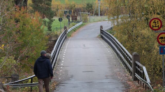 Linkoping, Sweden A man walks over a small bridge surrounded by autumn foliage. 
