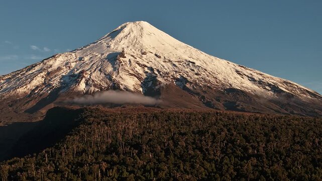 Sunrise light on snowy Villarrica volcano above forest, aerial