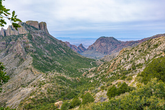 Winding trail cutting through a lush, green mountain pass flanked by rugged peaks under an overcast sky in West Texas.