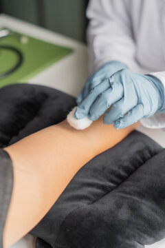 Doctor using cotton ball with antiseptic alcohol the area where blood will be drawn from the patient