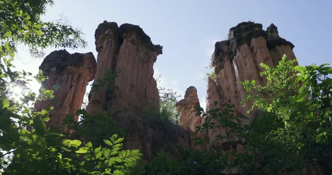 Low angle upward view reveals tall capped earth spires framed by green leaves at Pha Chor, Mae Wang National Park, Doi Lo, Chiang Mai, Thailand. Sunlight filters through forest around eroded pillars.