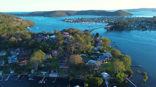 Drone aerial landscape of suburban residential housing and town wharfs along the Daleys Point waterfront foreshore with The Rip Bridge in the background near Booker Bay Central Coast Australia tourism