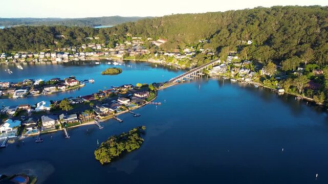 Drone aerial landscape of St Huberts Island Bridge and suburban housing along the waterfront foreshore surrounded by Brisbane Water and bushland forest trees at Daleys Point Central Coast Australia