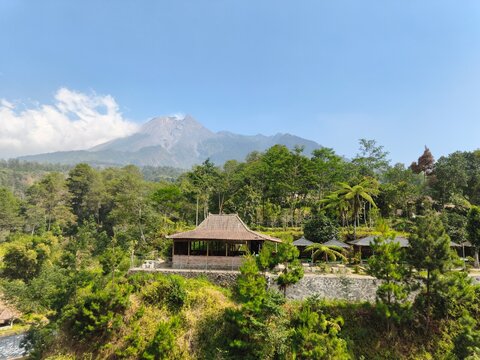 Lush Traditional Village Garden With Thatched Roof And Mount Merapi Volcano Under Blue Sky In Central Java Indonesia