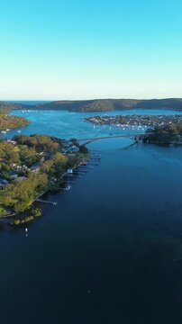 Drone aerial portrait of cars travelling on The Rip Bridge roadway surrounded by suburban housing and jetties along Brisbane Water near Daleys Point and Blackwall on the Central Coast NSW Australia