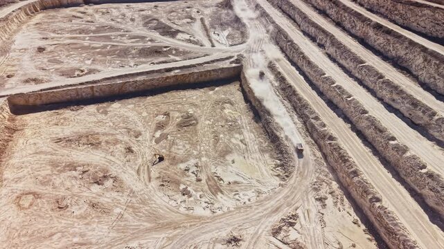 An overhead view shows quarry earthworks, with vehicle tracks and excavated lanes dividing sections of bare ground at the site during daylight.