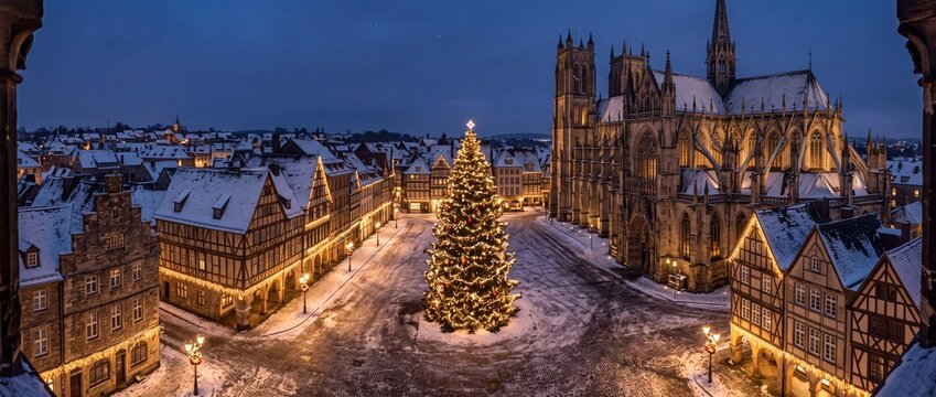 European town square decorated with glowing Christmas tree and snow covered medieval architecture at dusk