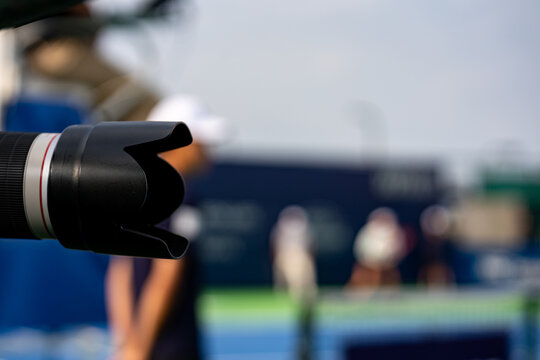 Close up of professional telephoto camera lens at tennis match.