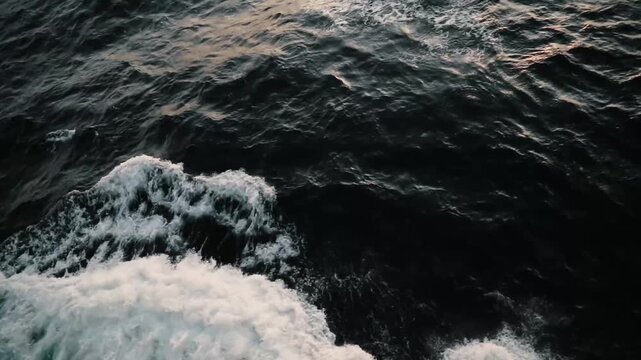 Aerial drone view of dark ocean waves crashing with white foam under golden-hour light