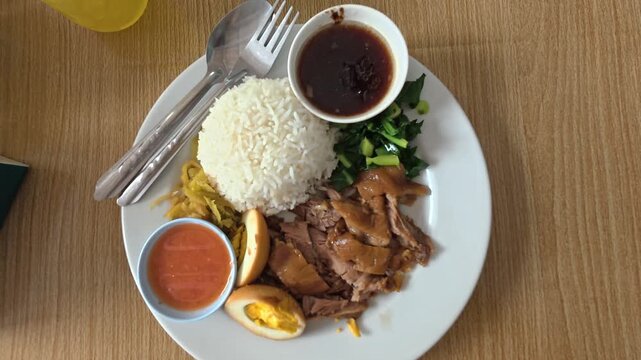 Overhead view dolly in and out to a plate of thai braised pork (Khao kha mu or khao kha moo) and egg with pickled cabbage, rice and steamed vegetables. An authentic traditional dish from Thailand