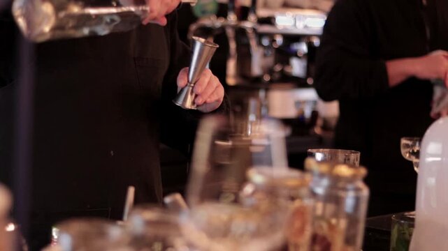 A glimpse of wine glasses, and in the background, some bartenders serving and preparing drinks at a nightclub. In the city. Nightlife. Parties and social gatherings.