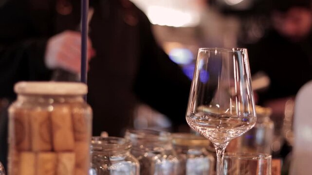 A glimpse of wine glasses, and in the background, some bartenders serving and preparing drinks at a nightclub. In the city. Nightlife. Parties and social gatherings.