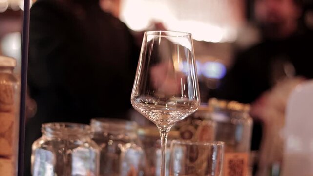 A glimpse of wine glasses, and in the background, some bartenders serving and preparing drinks at a nightclub. In the city. Nightlife. Parties and social gatherings.