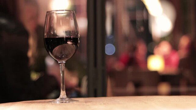 A glimpse of a wine glass, with shops and a brightly lit bar in the background. People enjoying themselves in the city. Nightlife. Parties and social gatherings.