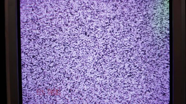 An old television, turned on but with no signal, gray static moving, varying in its image, a square, large, and well-maintained television