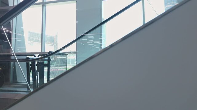 Smooth upward camera movement reveals intersecting escalator structures and expansive floor-to-ceiling windows inside a modern building, highlighting contemporary design and geometric lines.