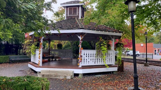 White wooden gazebo decorated for autumn surrounded by trees with fallen leaves on paved path  - Snoqualmie WA - October 10, 2026