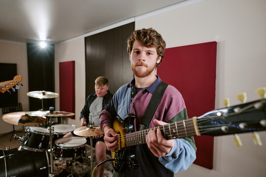 Portrait of young adult Caucasian man playing electric guitar during rock band rehearsal in recording studio. Image suitable for music production, band promotion and entertainment media