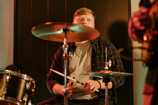Young adult Caucasian male drummer playing drum kit during live band performance. Useful for music festival marketing, concert promotion, entertainment media
