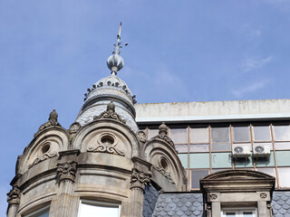Ornate old stone building corner with decorative dome, spire, carved details and round windows against a blue sky. Suitable for architecture, travel, history, tourism and European city themes © Evgeniia