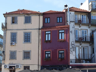 Old residential buildings with beige, burgundy and white facades, red tile roofs and balconies against a blue sky. Suitable for architecture, travel, real estate, tourism and European town themes. © Evgeniia